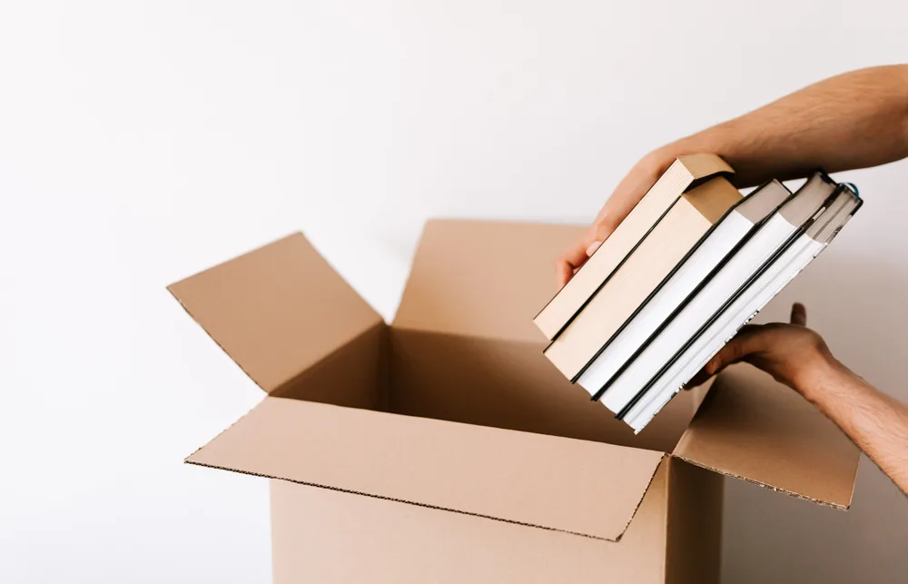 Des mains qui déposent une pile de livres dans un carton pour un don